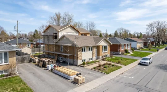 Bungalow résidentiel québécois en cours d'agrandissement avec échafaudage visible et matériaux de construction empilés dans l'allée